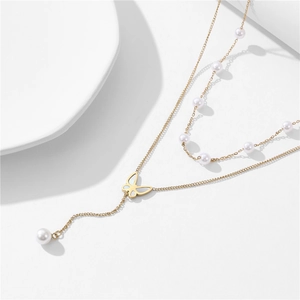 Double-layered gold butterfly necklace with delicate pearls on a white porcelain dish