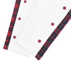 Detail of white trousers featuring red and green plaid trim and red decorative buttons