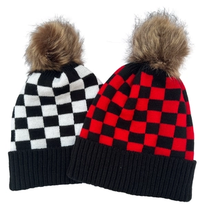 Close-up of winter knit beanies featuring plaid patterns and large faux fur pom-poms