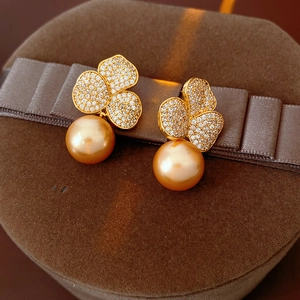 Close-up of gold-plated flower stud earrings with sparkling zircon and pearl drop