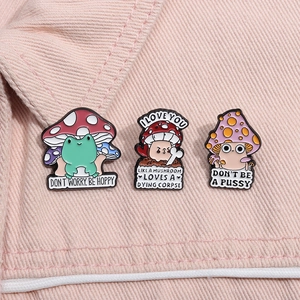 Detailed close-up of three cute enamel mushroom pins with slogans on pink denim fabric