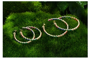 Detailed shot of two sizes of gold hoop earrings with multi-colored teardrop gemstones