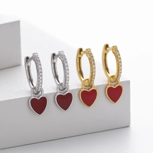 Detailed view of silver and gold heart earrings with red enamel and white zircon stones