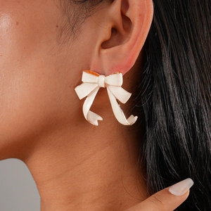 Close-up of elegant white enamel bow earrings with gold edges on model's ear