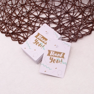 Stack of white cardstock thank you cards with gold foil lettering on a woven background