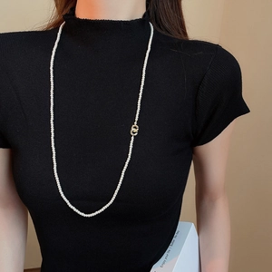 Detail of elegant pearl strand necklace with interlocking gold circles on a black sweater