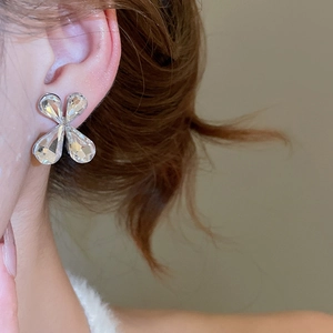 Macro view of a clover-shaped silver stud earring with clear crystals on a model's ear