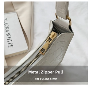 Close-up of golden zipper hardware and crocodile texture on white baguette bag