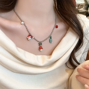 Detailed view of a Christmas themed necklace with bell and tree charms on a model's neck