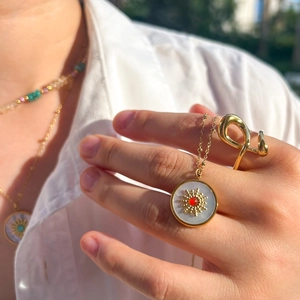 Golden sun necklace with red gemstone and white shell inlay worn in natural light