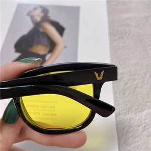 Detail of square black sunglasses with yellow lenses and gold V-shaped temple logo