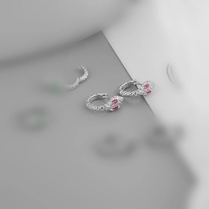 Close-up of silver snake earrings with pink gemstone eyes in minimalist style
