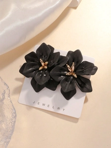 Macro detail of black acrylic flower earrings with gold center on a white card