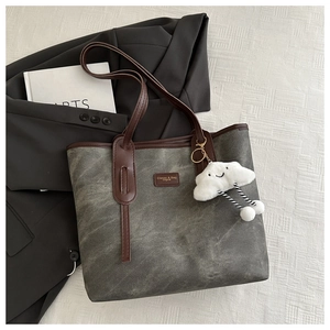 Detail of grey tote bag featuring brown faux leather handles and a cute cloud charm accessory