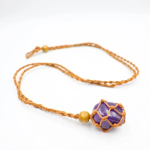 Macro shot of a raw purple amethyst stone secured in a handmade brown woven cord mesh pouch