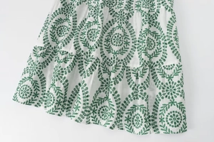 Nahaufnahme der grünen Blumenstickerei und der Stufenstruktur auf dem weißen Kleid