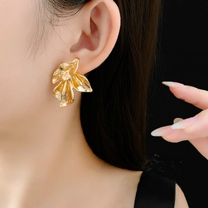 Gros plan d'une boucle d'oreille feuille dorée portée par un mannequin sur fond noir