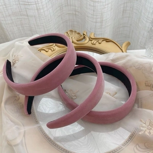 Gros plan de trois serre-têtes en velours rose sur un fond de tissu brodé blanc