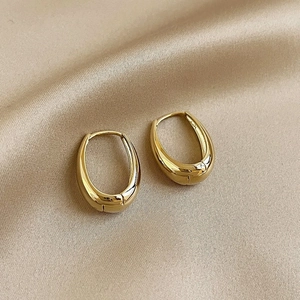Detailed view of polished golden teardrop hoop earrings resting on champagne silk fabric