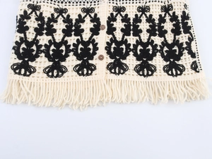 Detail of bohemian crochet vest with floral patterns, wooden buttons and tassel hemline
