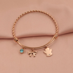 Detail of rose gold twist bangle with angel, bow, and light blue gemstone charms