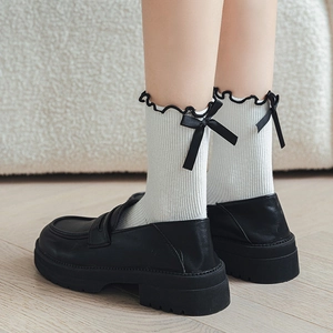 Detail of white ribbed mid-calf socks with black ruffle trim and bows paired with loafers