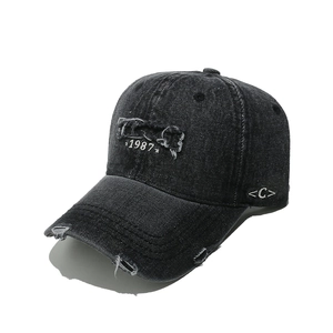 Detailed shot of black distressed denim baseball cap with 1987 embroidery and ripped edges