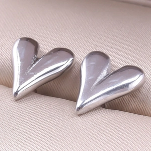 Detailed close-up of polished silver heart earrings on a champagne jewelry box liner