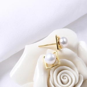 Elegant square gold earrings with white natural pearls on a white ceramic flower