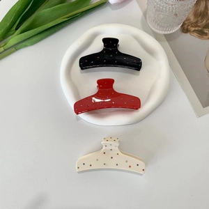 Three acetate hair claws in black, red, and beige with colorful polka dots on a table
