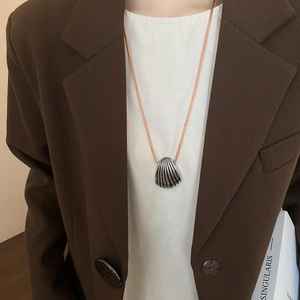 Detailed view of silver shell pendant with orange cord on a model with blazer