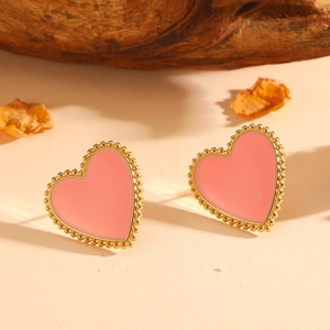 Detail of heart-shaped gold studs with pink enamel and milgrain edges on a textured surface