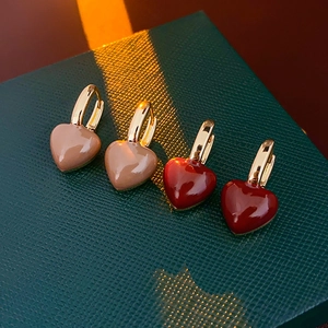 Detail of gold-plated heart earrings in pink and burgundy enamel on a textured green box