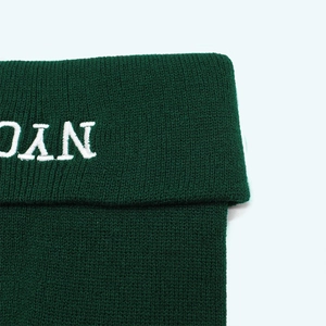 Close-up of white NYC embroidery on forest green ribbed knit beanie with precise stitching