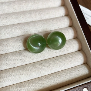Close-up of vintage green round earrings displayed in a luxury beige cushioned jewelry box