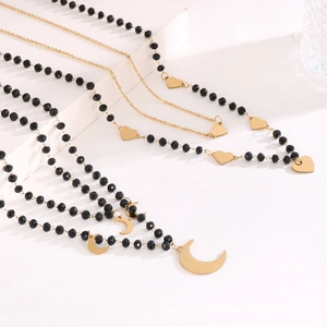 Detail of layered gold chains with heart charms and black bead moon pendant necklace