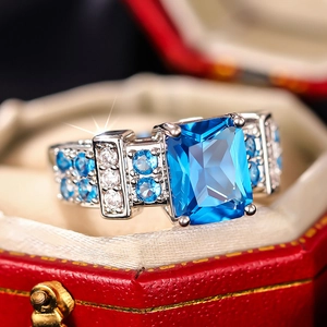 Macro detail of a square blue gemstone ring with micro-pave setting in a red velvet box