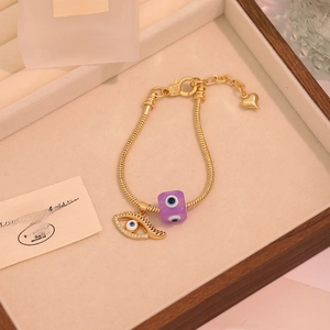 Detail of gold snake chain bracelet with evil eye charm and purple beads in a gift box