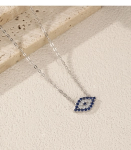 Macro shot of silver Evil Eye necklace with blue stones on a natural beige stone background