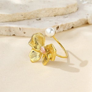 Detail of gold bow ring with pink gemstone and white pearl on a natural stone base