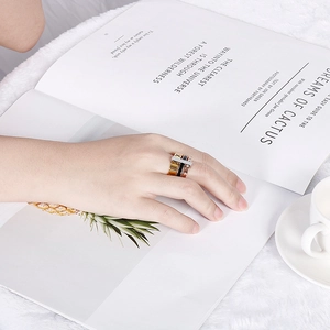 Close-up of three-piece stacked roman numeral rings in gold, black and rose gold finish