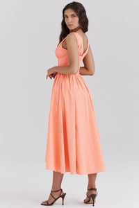 Side profile of coral orange sleeveless maxi dress with a cinched waist and pleated skirt