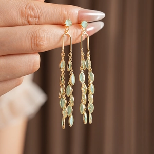 Détail de boucles d'oreilles pompons dorées avec feuilles en opale et longues chaînes