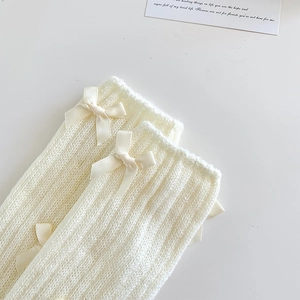 Détail de jambières en tricot côtelé crème avec trois nœuds décoratifs en satin