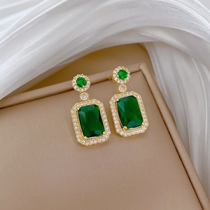 Macro detail of gold-plated earrings featuring emerald green stones and zircon pavé