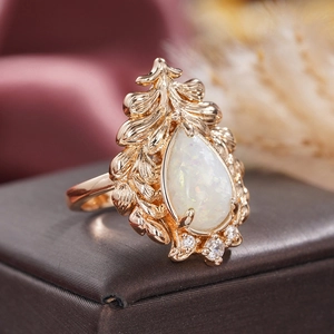 Macro shot of rose gold ring featuring pear-shaped opal and leaf motif on jewelry box