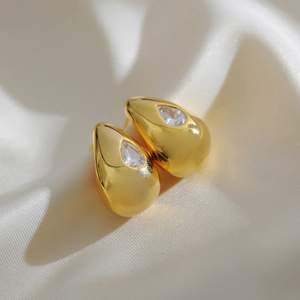 Macro shot of gold teardrop earring featuring a pear-cut cubic zirconia on white silk