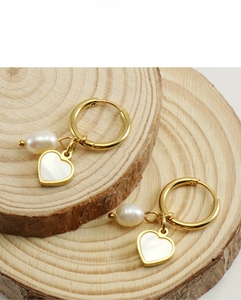 Détail de boucles d'oreilles cœur en nacre avec perles et anneau doré sur bois