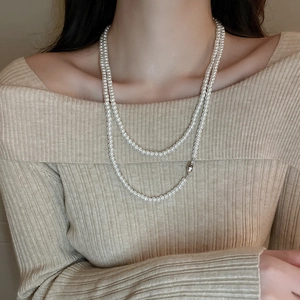 Nahaufnahme einer zweilagigen weißen Perlenkette, kombiniert mit beigem Strickoberteil