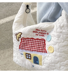 Close-up of white quilted tote bag featuring house embroidery and plush bird detail